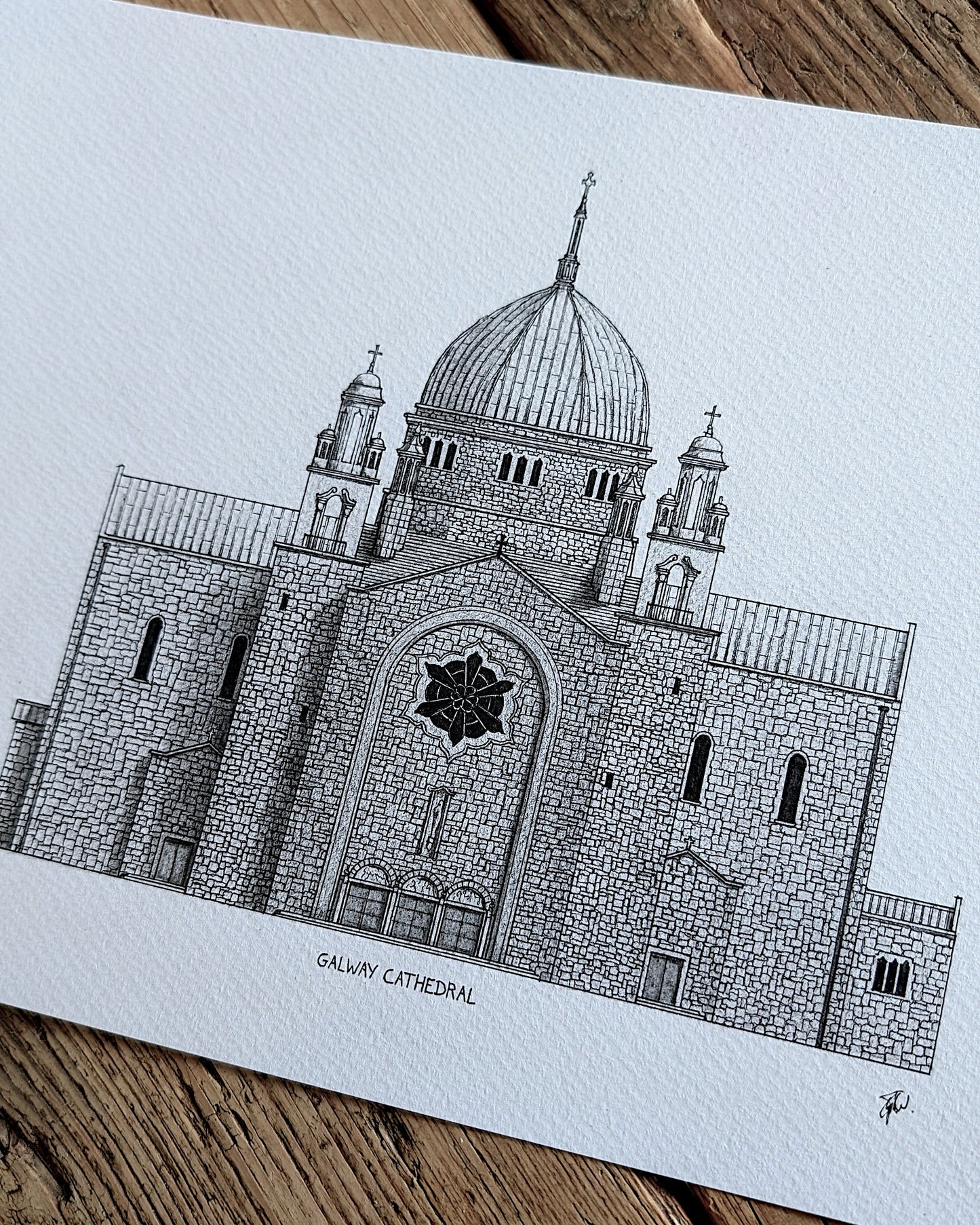 A black and white architectural art print of the Galway Cathedral, displayed on a rustic wooden surface.