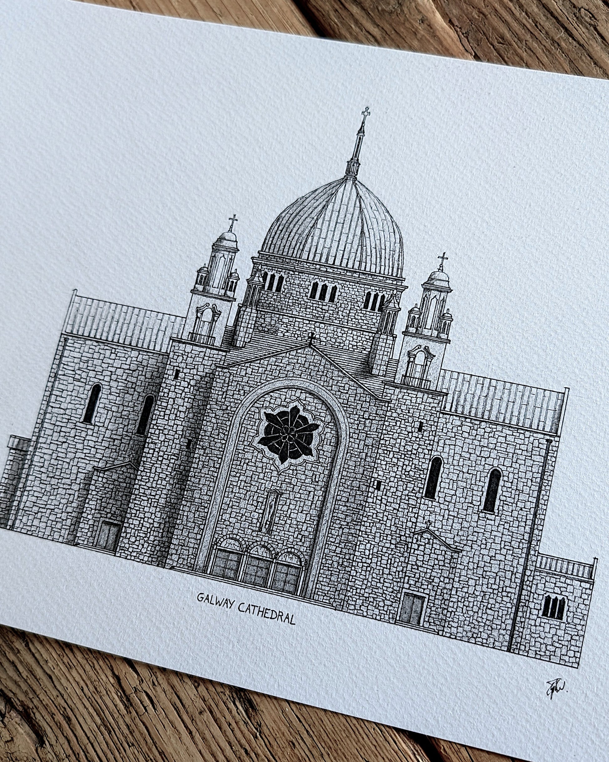 A black and white architectural art print of the Galway Cathedral, displayed on a rustic wooden surface.