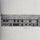 A black and white architectural art print of 'Tudor Barn, Eltham' resting on a rustic wooden surface.