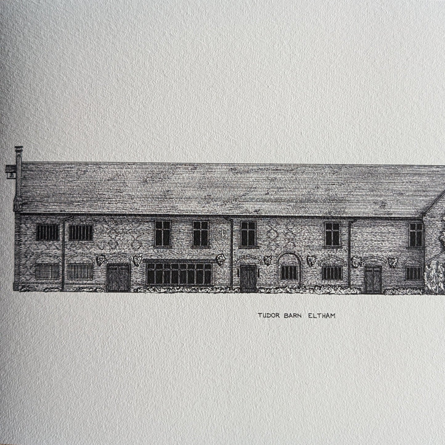 A black and white architectural art print of 'Tudor Barn, Eltham' resting on a rustic wooden surface.